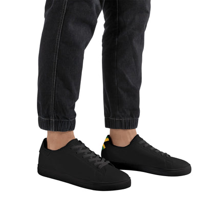 All-black Jamaica flag Ackee Walkers low top sneakers with black laces, black outsole and a green and gold Jamaican flag chevron at the heel