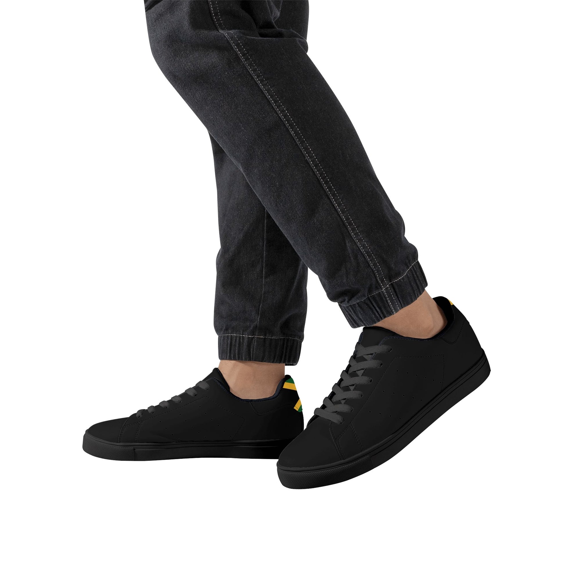 All-black Jamaica flag Ackee Walkers low top sneakers with black laces, black outsole and a green and gold Jamaican flag chevron at the heel