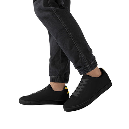 All-black Jamaica flag Ackee Walkers low top sneakers with black laces, black outsole and a green and gold Jamaican flag chevron at the heel