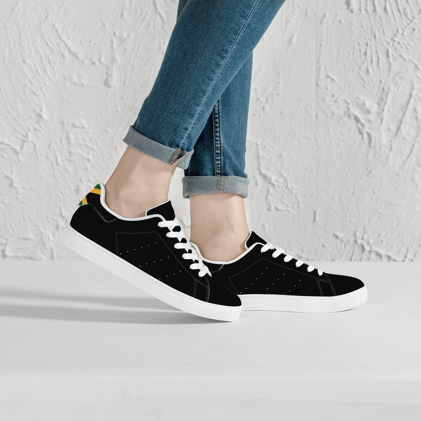 All-black Jamaica flag Ackee Walkers low top sneakers with black laces, black outsole and a green and gold Jamaican flag chevron at the heel