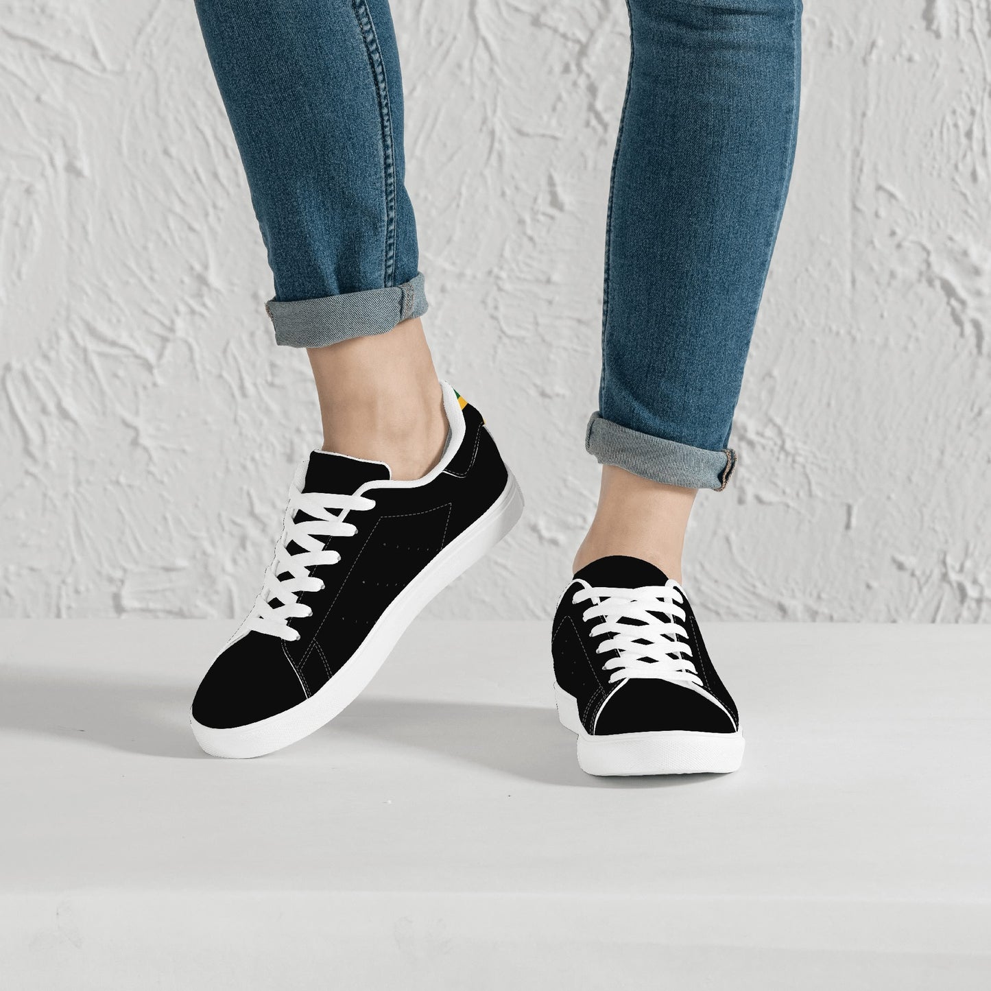All-black Jamaica flag Ackee Walkers low top sneakers with black laces, black outsole and a green and gold Jamaican flag chevron at the heel