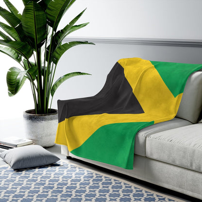 Jamaican flag blanket folded across the arm of a light grey sofa beside a tall potted plant.