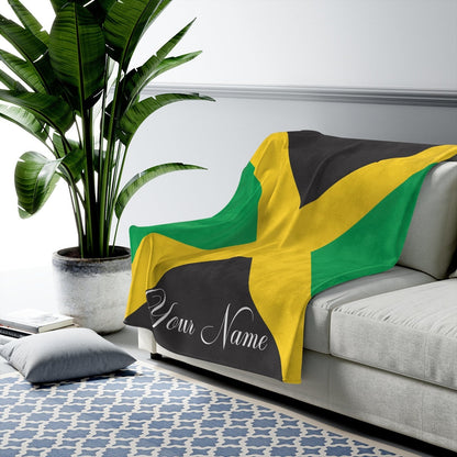 Jamaica flag fleece blanket draped over a grey sofa with a name in white script on the black panel.